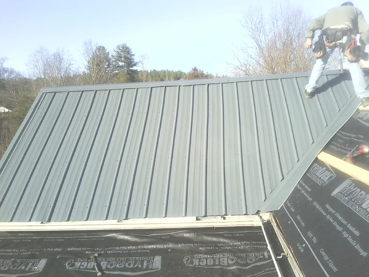 Crew installing dark green standing seam panels over synthetic underlayment in Vallejo